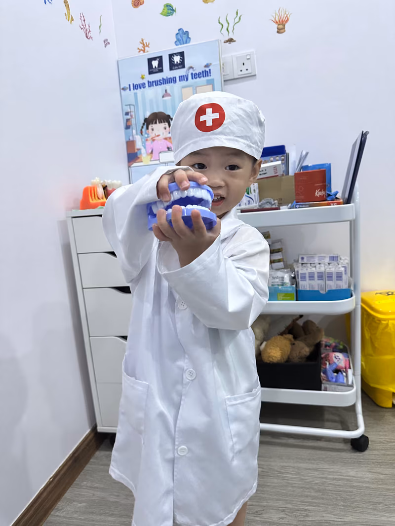 Young child dressed as a dentist holding a tooth model in a fun and friendly pediatric dental clinic environment.
