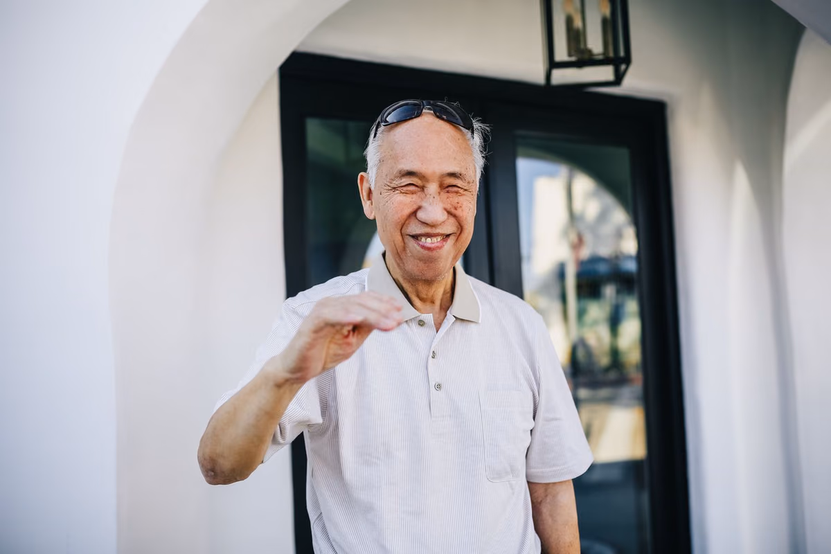 An older man smiling in a doorway, the age group most often told they need bone grafting before a dental implant can be placed.
