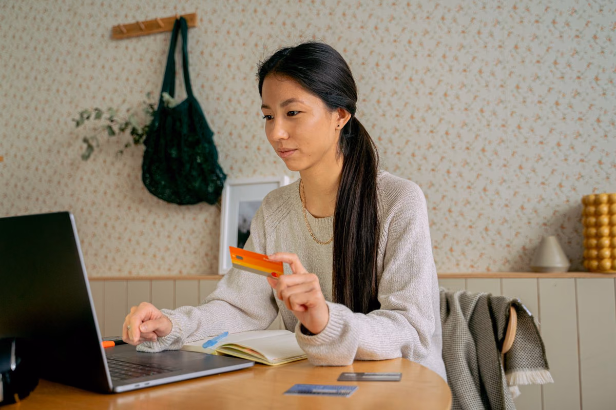 A woman at a laptop holding a credit card, arranging staged payments for dental treatment from home in Malaysia.