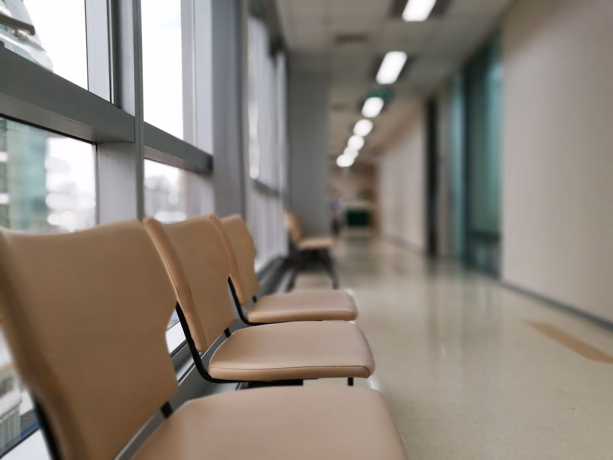 A row of empty chairs along a quiet hospital corridor, representing the waiting list involved in getting dental implants through a government hospital in Malaysia.