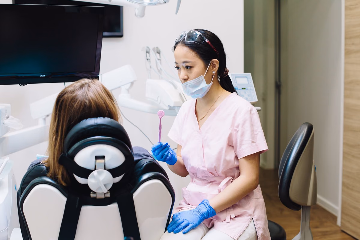 A dentist in a Kuala Lumpur clinic talking a seated patient through treatment options, the conversation that should happen before committing to Invisalign.