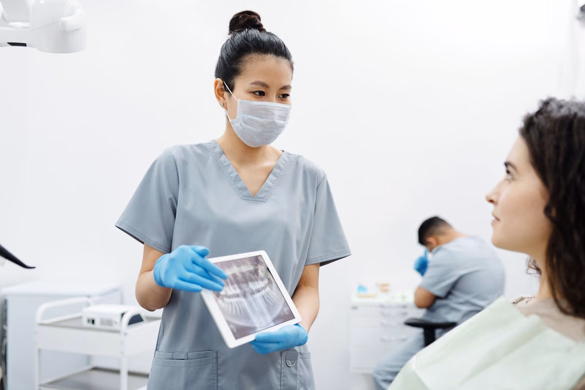 A dentist showing a patient their dental X-ray on a tablet, the diagnostic step that reveals how complex a case is and what it will cost.