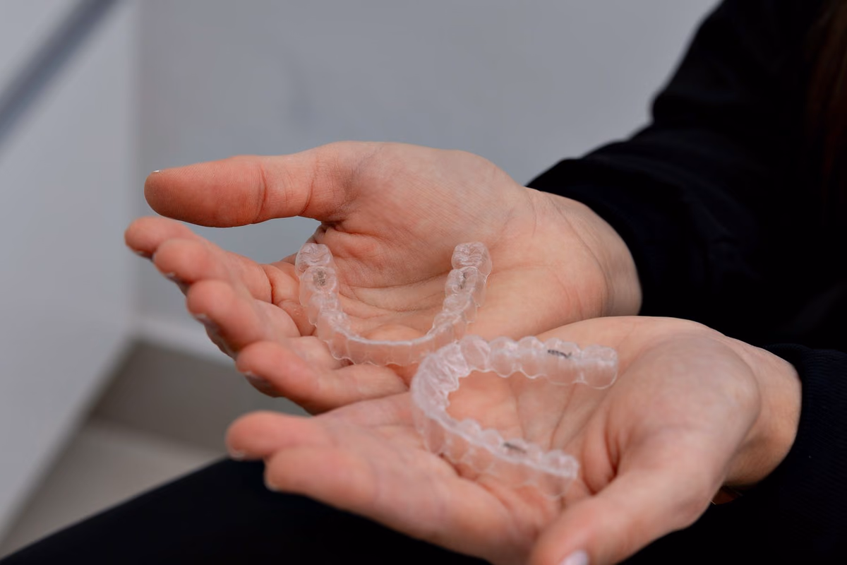 Clear Invisalign aligner trays held in a gloved hand at a dental clinic, illustrating a full Invisalign course in Kuala Lumpur.