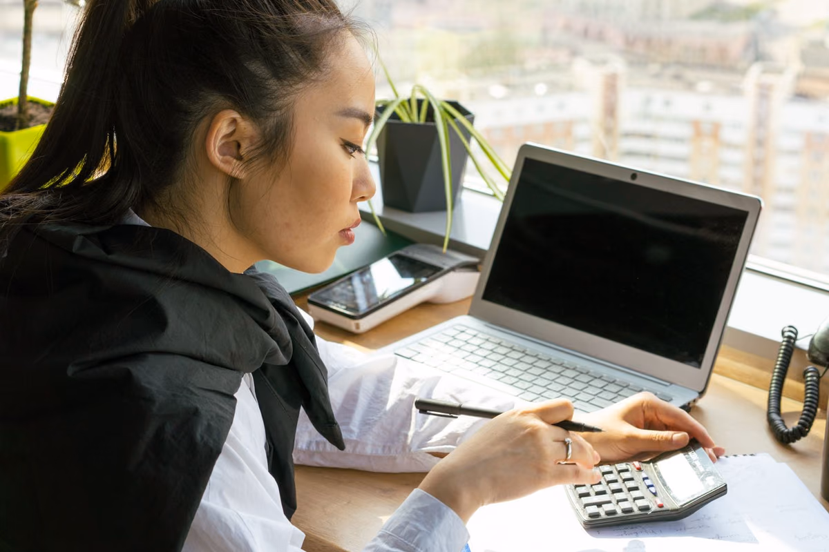 A woman calculating treatment costs on a laptop and calculator, the budgeting that usually decides between fixed braces and clear aligners.