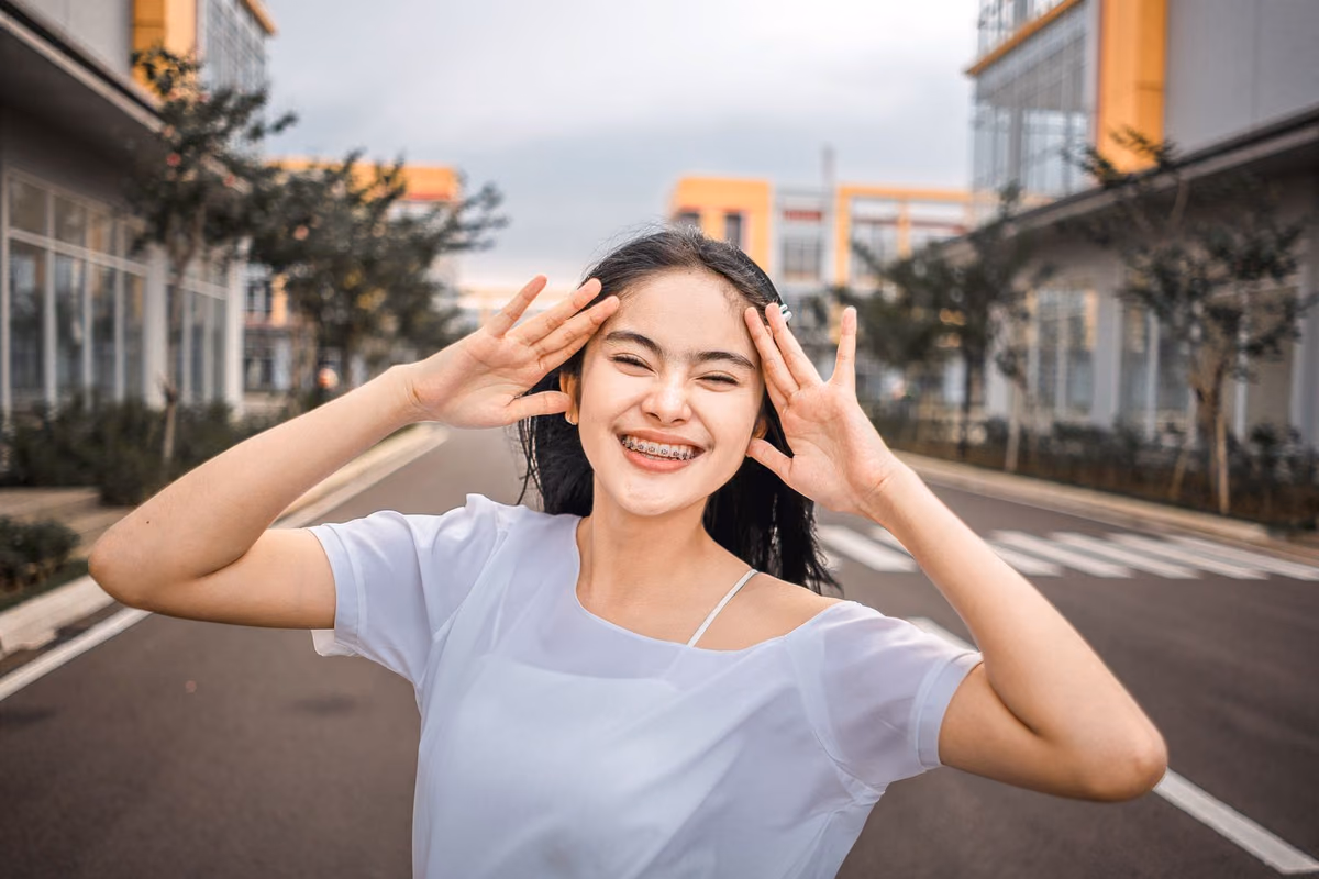 A young woman smiling openly while wearing fixed orthodontic braces, one of the two main teeth-straightening routes available in Malaysia.