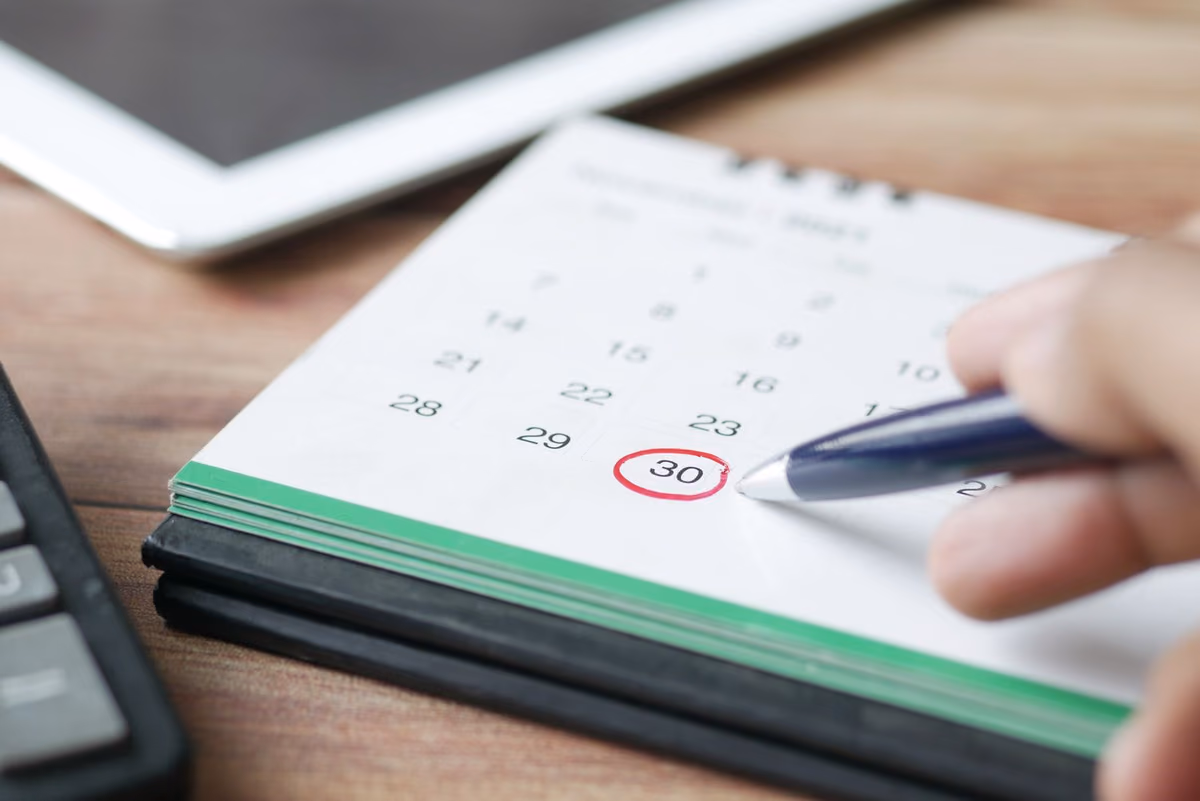 A hand marking a date on a wall calendar, representing the treatment timeline patients weigh when choosing between aligners and fixed braces.