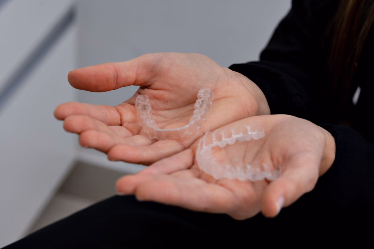 Close-up of hands holding a set of transparent removable aligner trays in a dental clinic, the treatment most Malaysians mean by invisible braces.