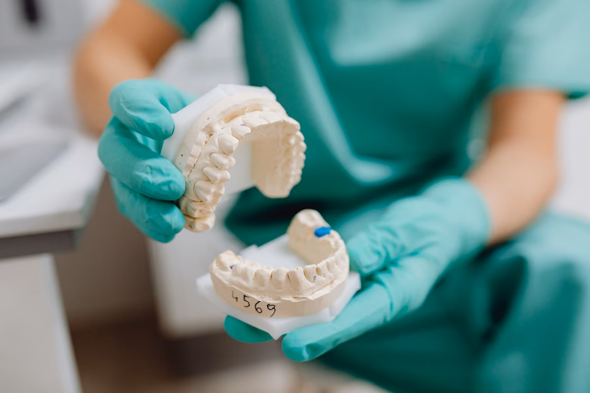 A gloved hand holding a plaster dental cast in a clinic, representing the physical assessment and records taken before orthodontic treatment begins.