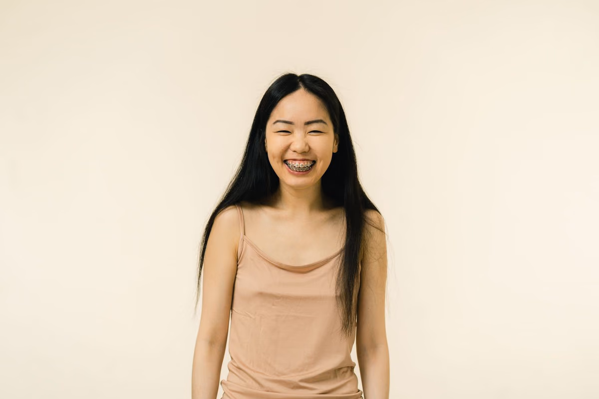 A young woman smiling confidently while wearing orthodontic braces, showing how visible fixed appliances are compared with discreet alternatives.